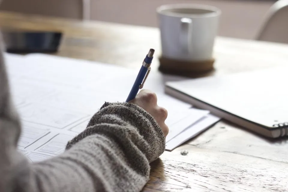 Mano escribiendo en un cuaderno junto a una taza de café